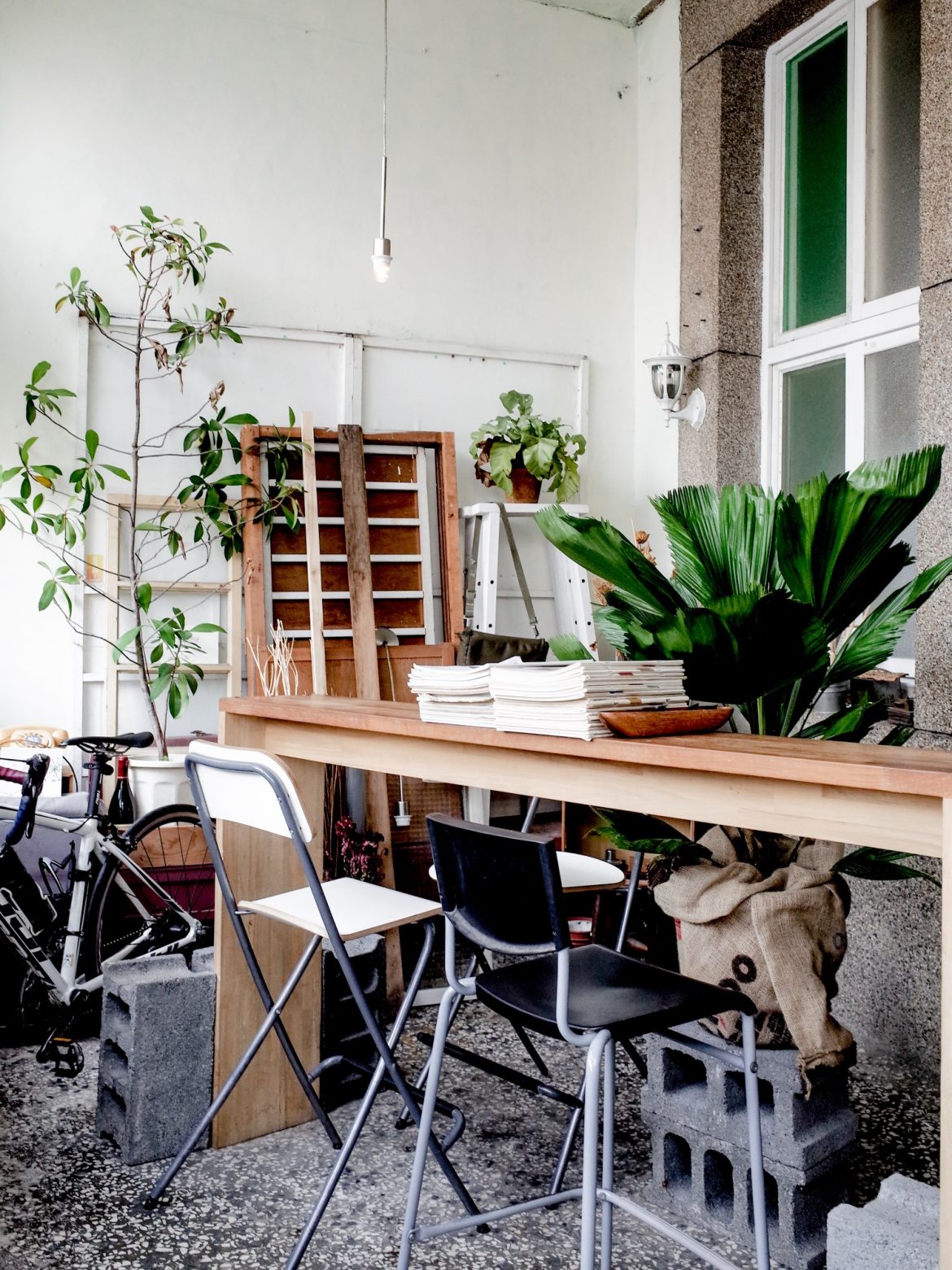 前院的小小座檯，一旁堆疊著木窗與工具，在大量綠色植栽環繞下，竟也有種庭院工作室般的舒適感。