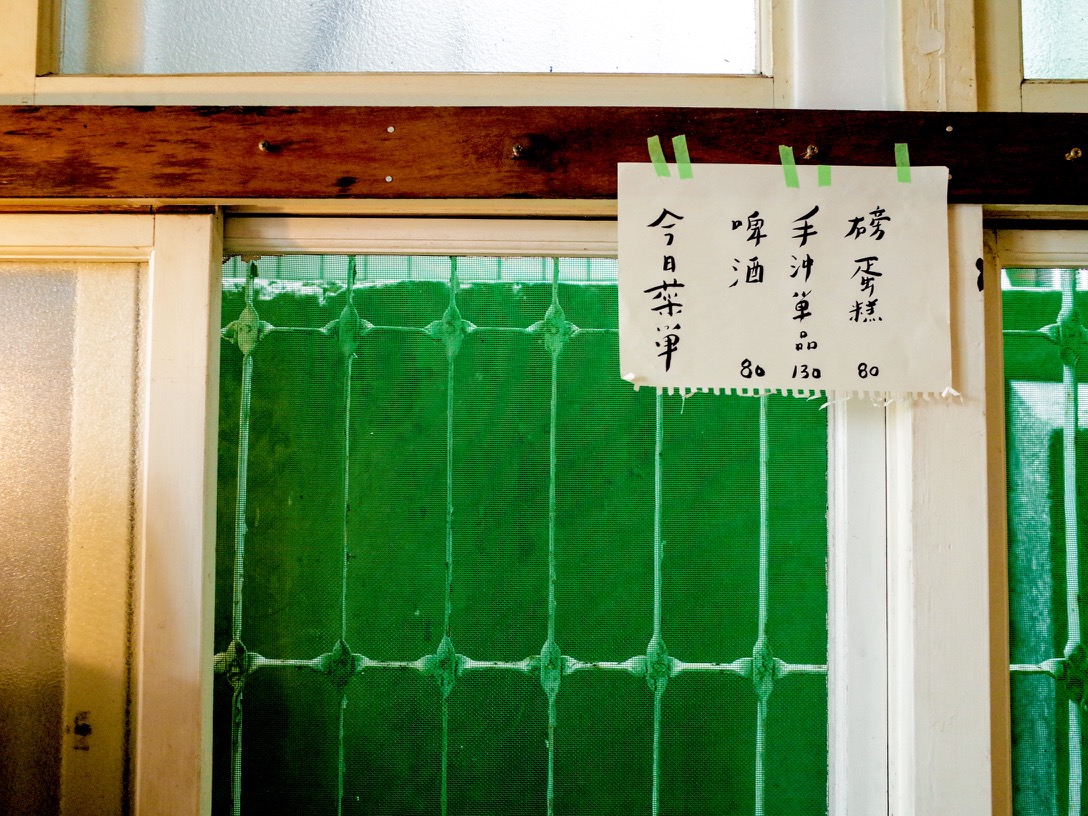 手寫菜單以綠色紙膠帶隨性貼黏在窗框，老舊的綠色紗窗成了最古早味的背景。